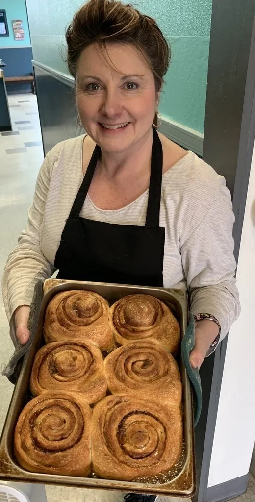 Sherri McVey smiling, holding a fresh tray of cinnamon rolls
